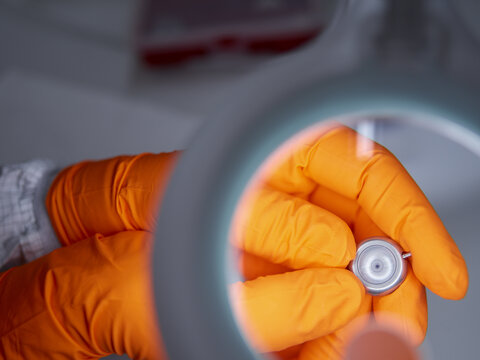 Hände mit orangen Handschuhen präsentieren ein Bohrlochumlenker unter einem Mikroskob